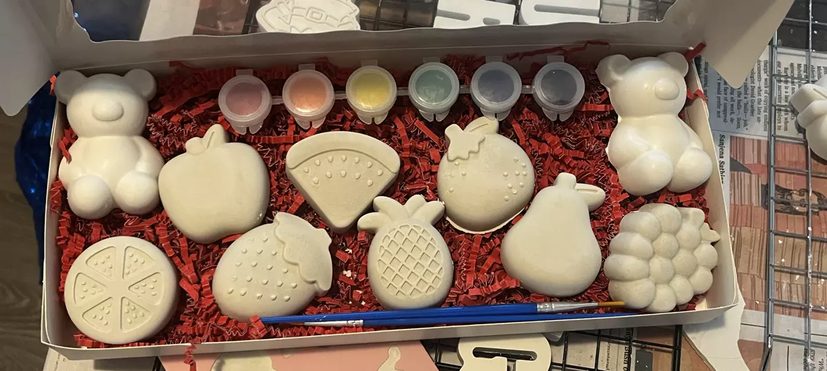 Open box of plaster teddy bears and fruit shapes packed in red paper with paint and one brush