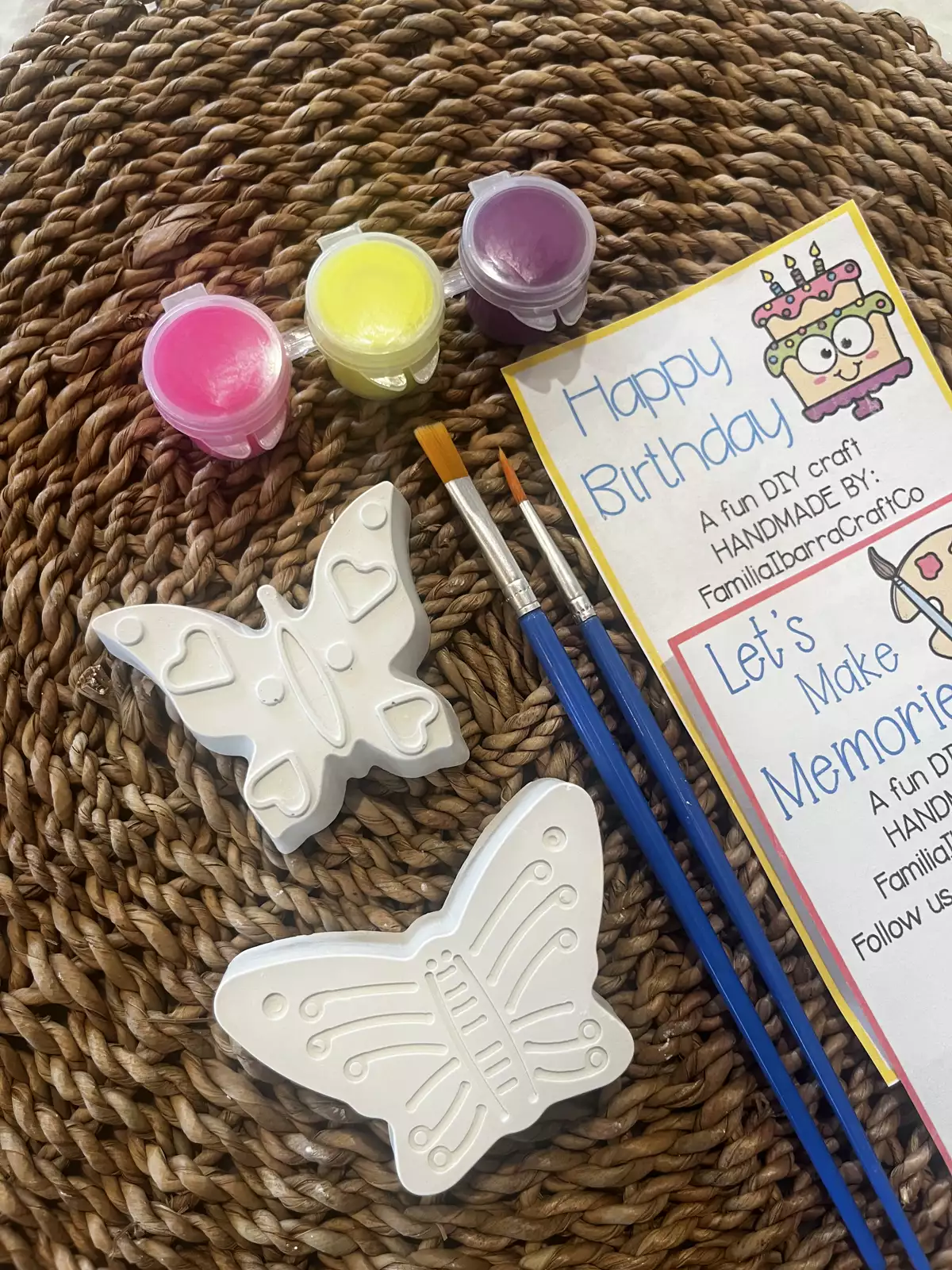 Two white plaster butterflies with three pots of paint and two brushes