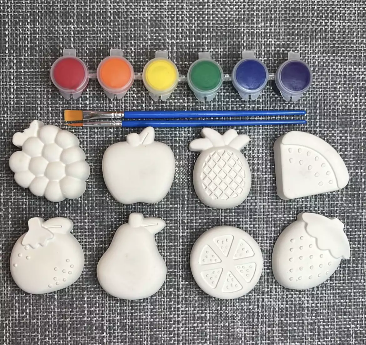 Plaster fruit shapes, including grapes, an apple, a pineapple, and a strawberry, with paint and brushes